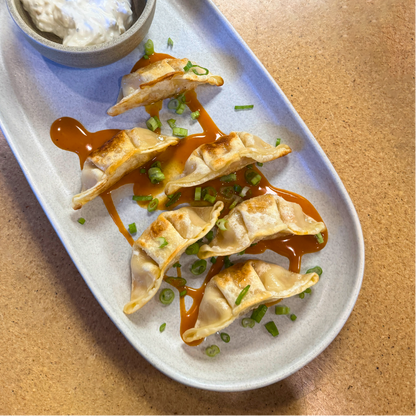 Platter of dumplings with dipping sauce and garnish on a wooden surface